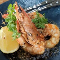 Succulent grilled prawns with garlic and herbs, served with lemon and sesame seeds in a dark sauce.