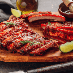 Smoked ribs with BBQ sauce, lime, and herbs on a wooden platter for wine and food pairing.