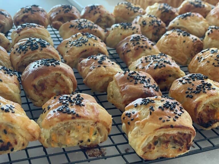 Fresh sausage rolls with flaky pastry and black sesame seeds, perfect for wine and food pairing.