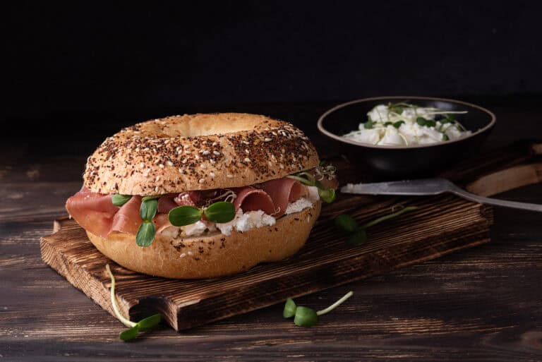 Fresh Bagel Sandwich with Prosciutto and Microgreens on Wooden Board, Delicious Food.