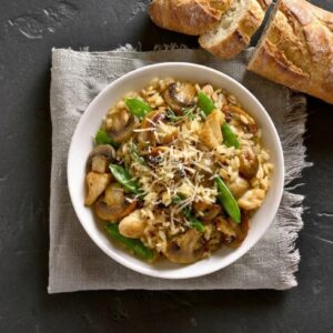 Baked chicken mushroom risotto with leek and thyme served in a white bowl on dark slate