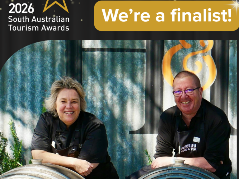 Jackie and John leaning on wine barrels under the We are a finalist badge for the 2026 South Australian Tourism Awards