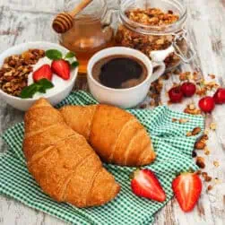 Freshly baked croissants with strawberries, granola, honey, and coffee, showcasing Fleurieu Food & Wine.