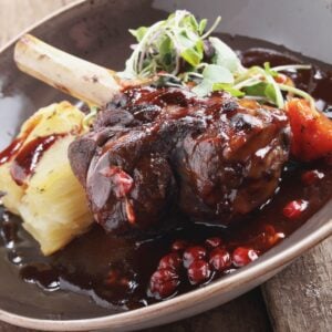 Braised lamb shank with roasted potatoes and pomegranate on a rustic ceramic plate