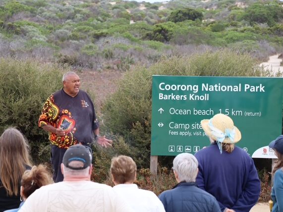 Ngarrindjeri Elder Mark Koolmatrie speaking to a group of visitors beside the Barkers Knoll sign in Coorong National Park