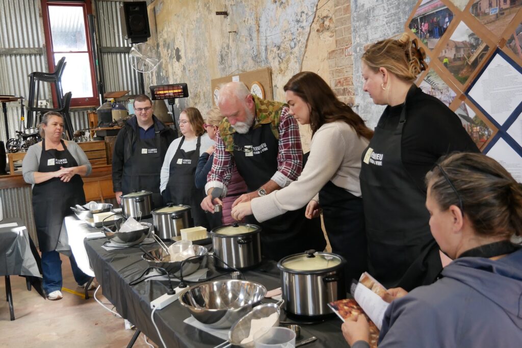Guests in aprons watch cheese curd being stretched at a long table in the Milang Lakeside Butter Factory