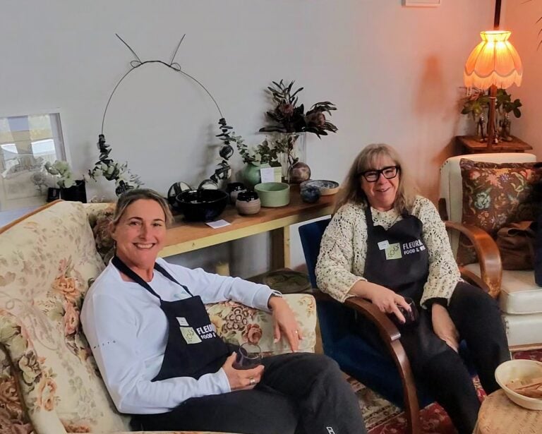 Two guests in Fleurieu Food and Wine aprons relaxing in armchairs with a glass of red wine after a gnocchi cooking class at Lot 50, Yankalilla