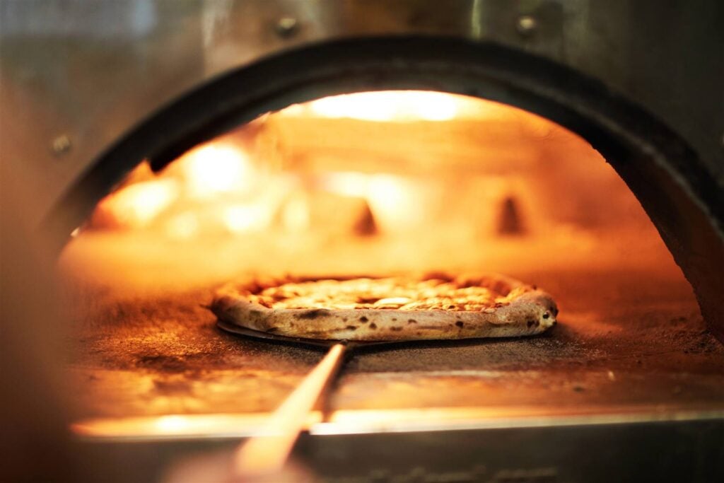 A pizza blistering and cooking inside a glowing wood-fired oven