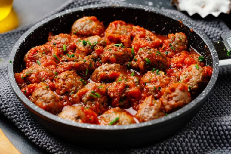 Sautéed meatballs in rich tomato sauce, garnished with fresh herbs, served in a black skillet.