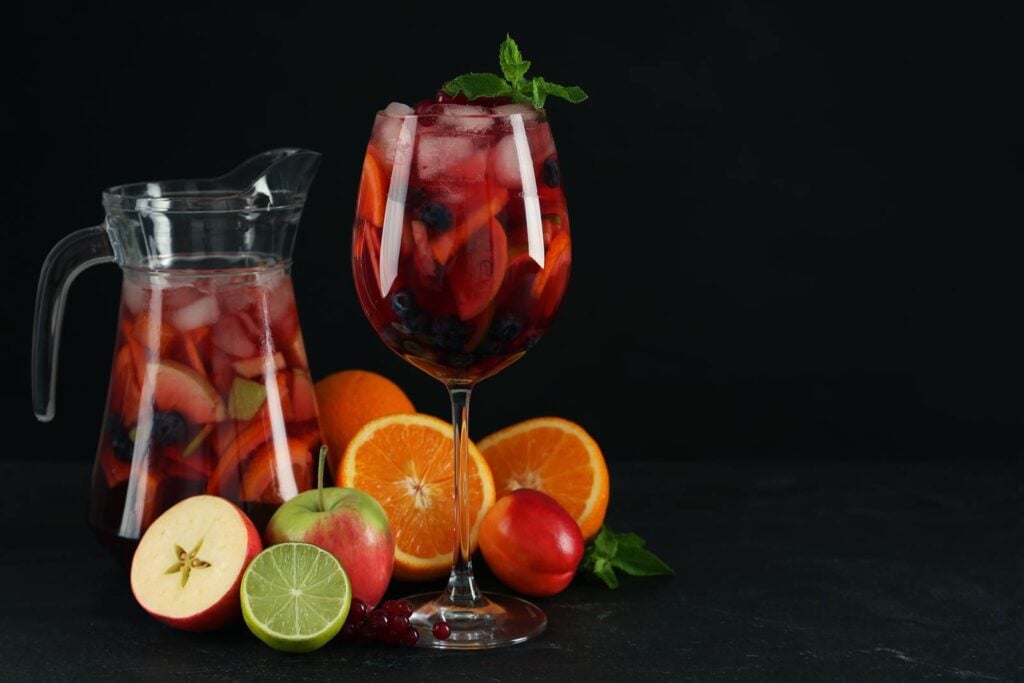 A jug and glass of red sangria with orange, apple and berries