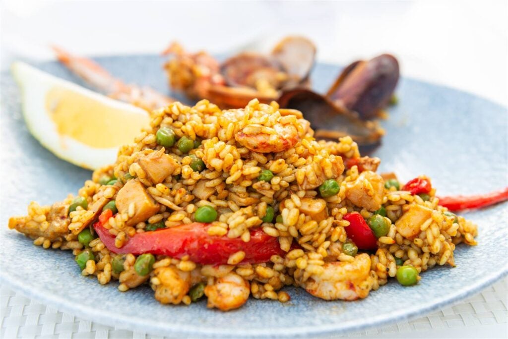 A plate of seafood paella with prawns, mussels, peas and lemon