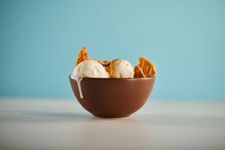 Creamy vanilla ice cream with caramel sauce and waffle cones in a brown bowl.