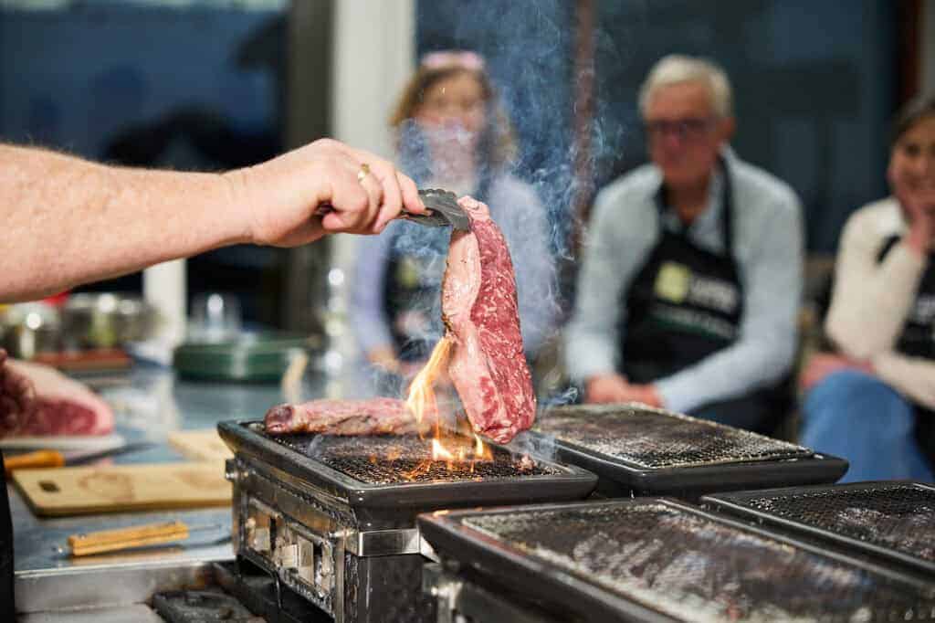 Steak lifted with tongs over the flaming hibachi grill during the Steak Masterclass