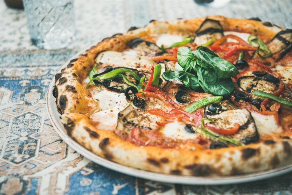A wood-fired vegetable pizza topped with peppers, olives and fresh basil on a plate